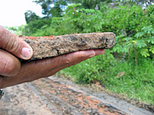 Zerbrochener Asphalt und Stück, welches die Dicke der Asphaltschicht zeigt